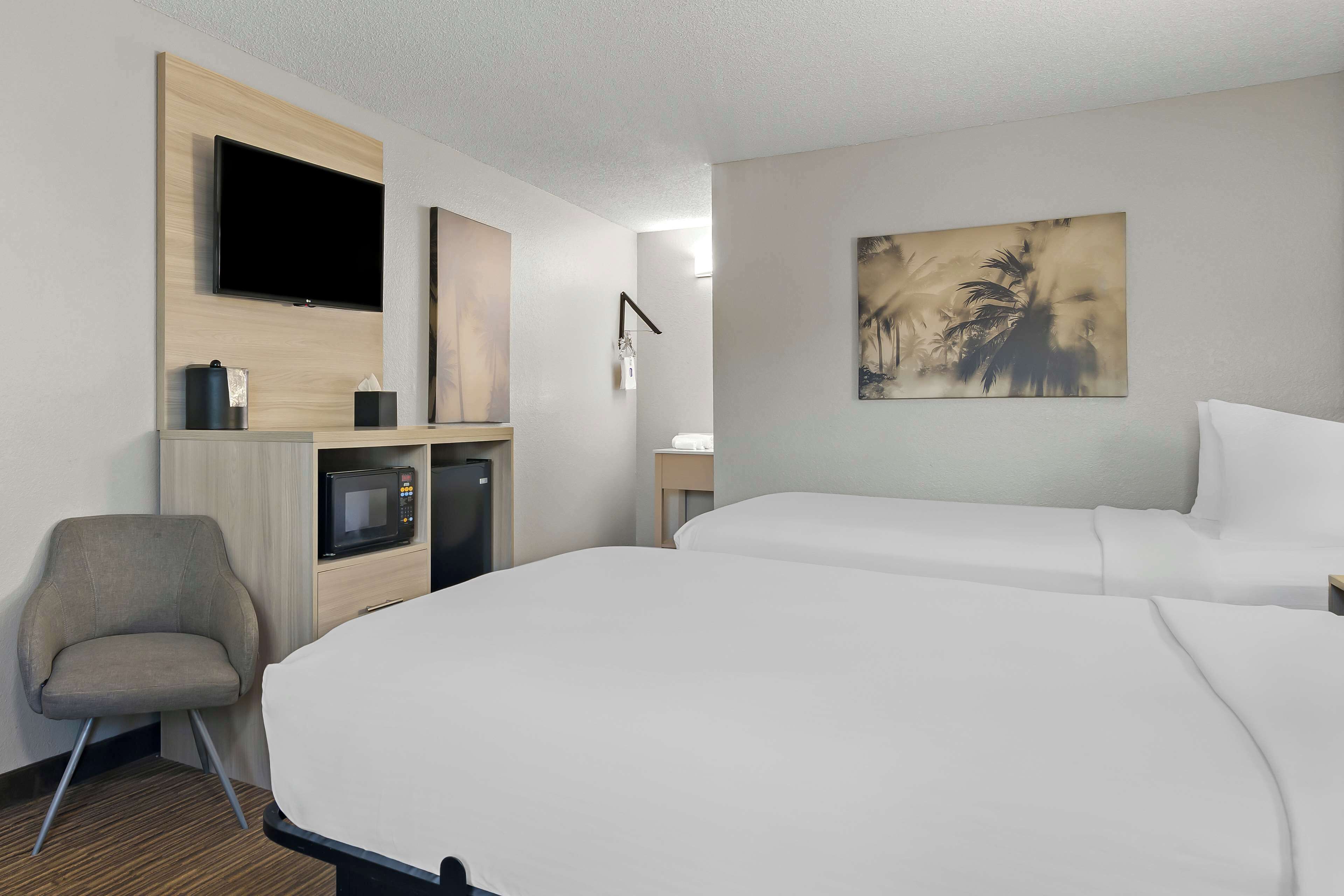 Une chambre d’hôtel avec deux lits, une télévision, un four à micro-ondes, une chaise et un tableau au mur.
