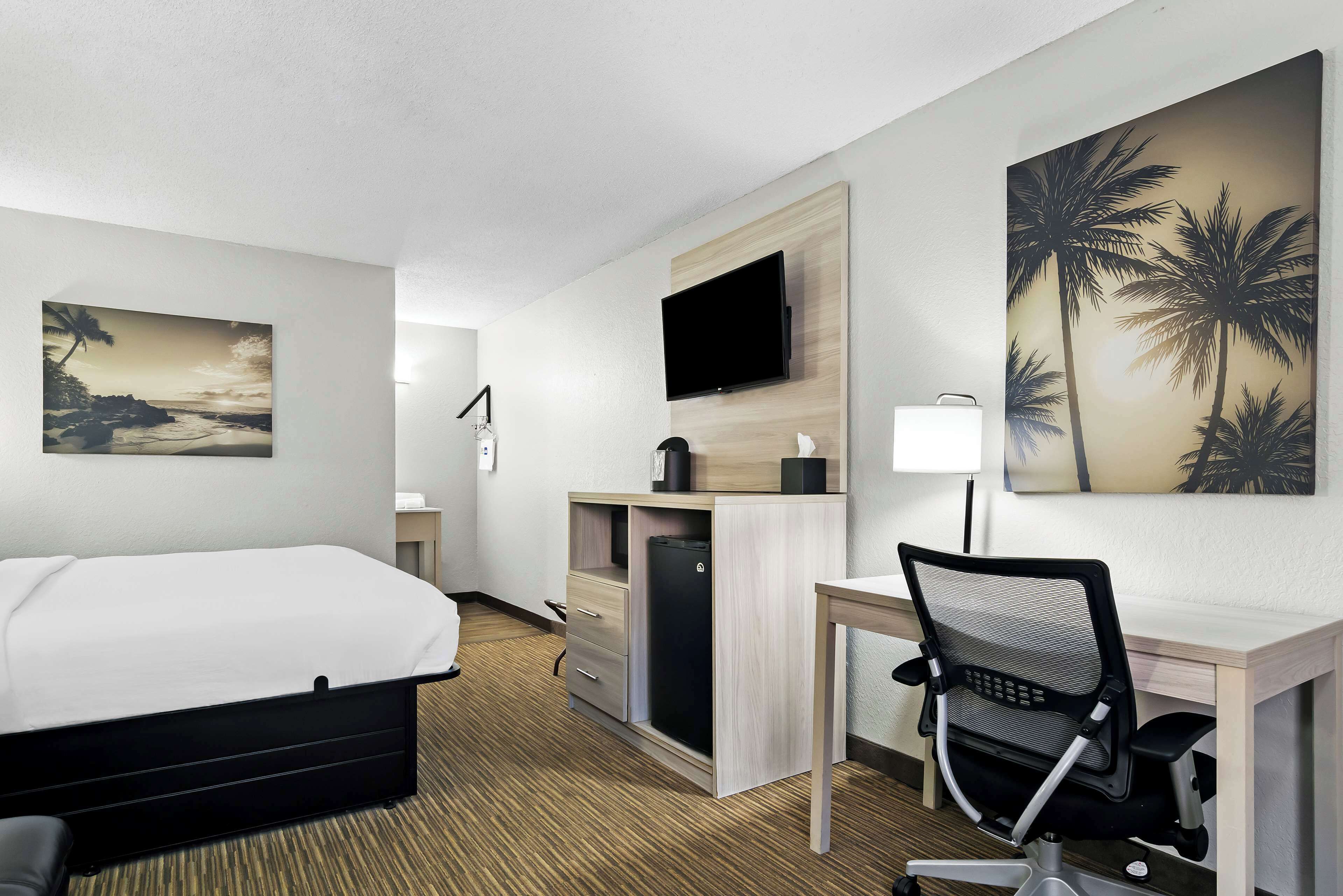 Habitación de hotel con cama, escritorio, silla, televisión y obras de arte.