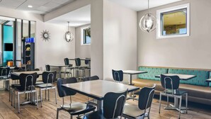 Un comedor moderno con varias mesas y sillas, piso de madera y un área de estar color turquesa.
