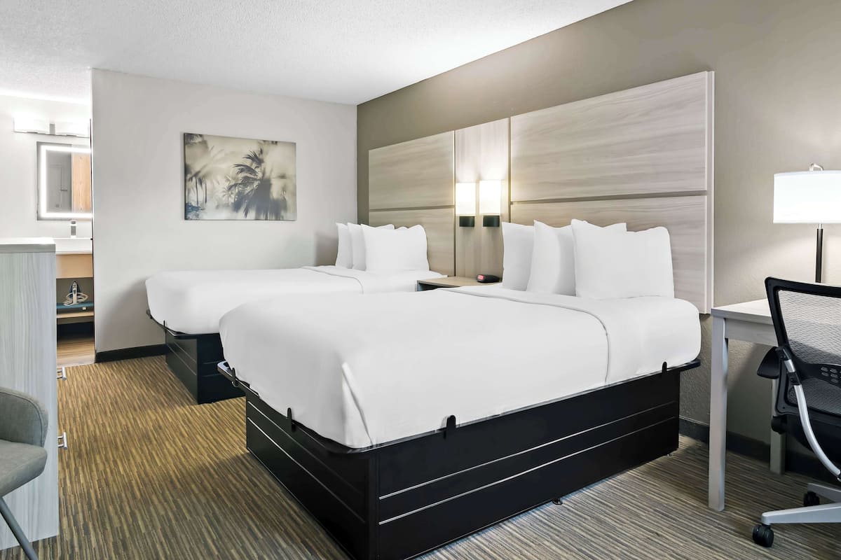 Een hotelkamer met twee bedden, een bureau, een stoel en een in de achtergrond zichtbare badkamer.