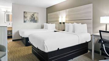 A hotel room with two beds, a desk, a chair, and a bathroom visible in the background.