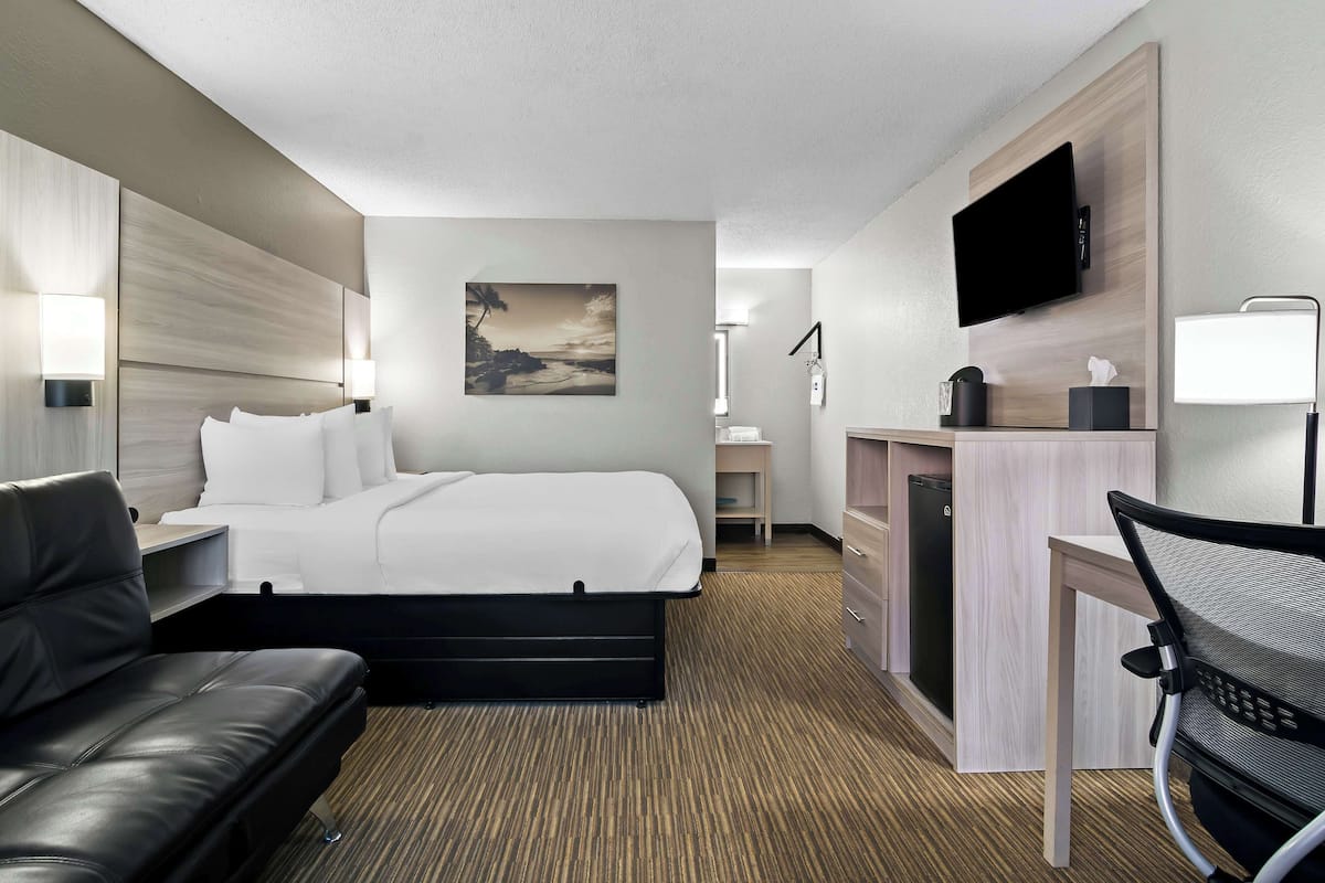 Een hotelkamer met een bed, een bureau, een stoel, een televisie en een schilderij aan de muur.