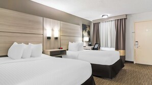 Una habitación de hotel con dos camas, un escritorio, una lámpara y una puerta.