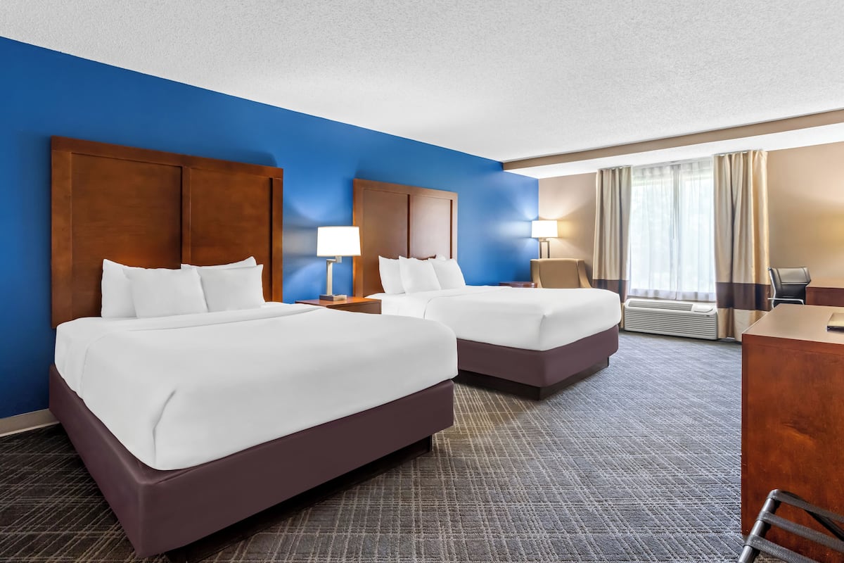 A hotel room with two beds, a desk, and a chair.