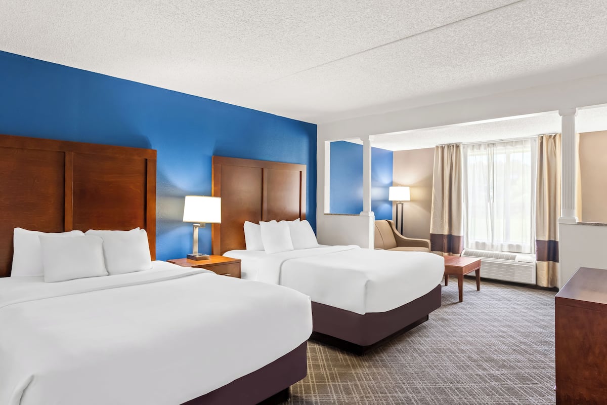 A hotel room with two beds, a desk, a chair, and a large window with curtains.