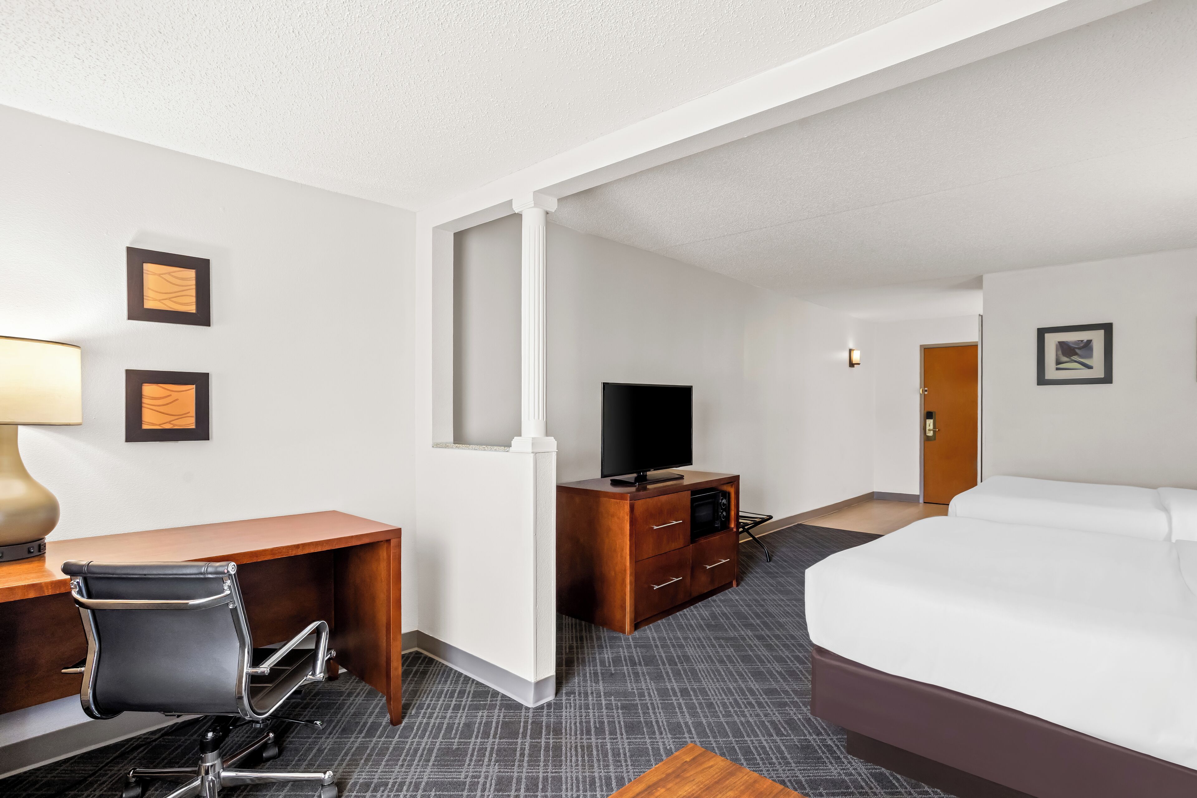 Una habitación de hotel con cama, escritorio, silla, televisión y cómoda.