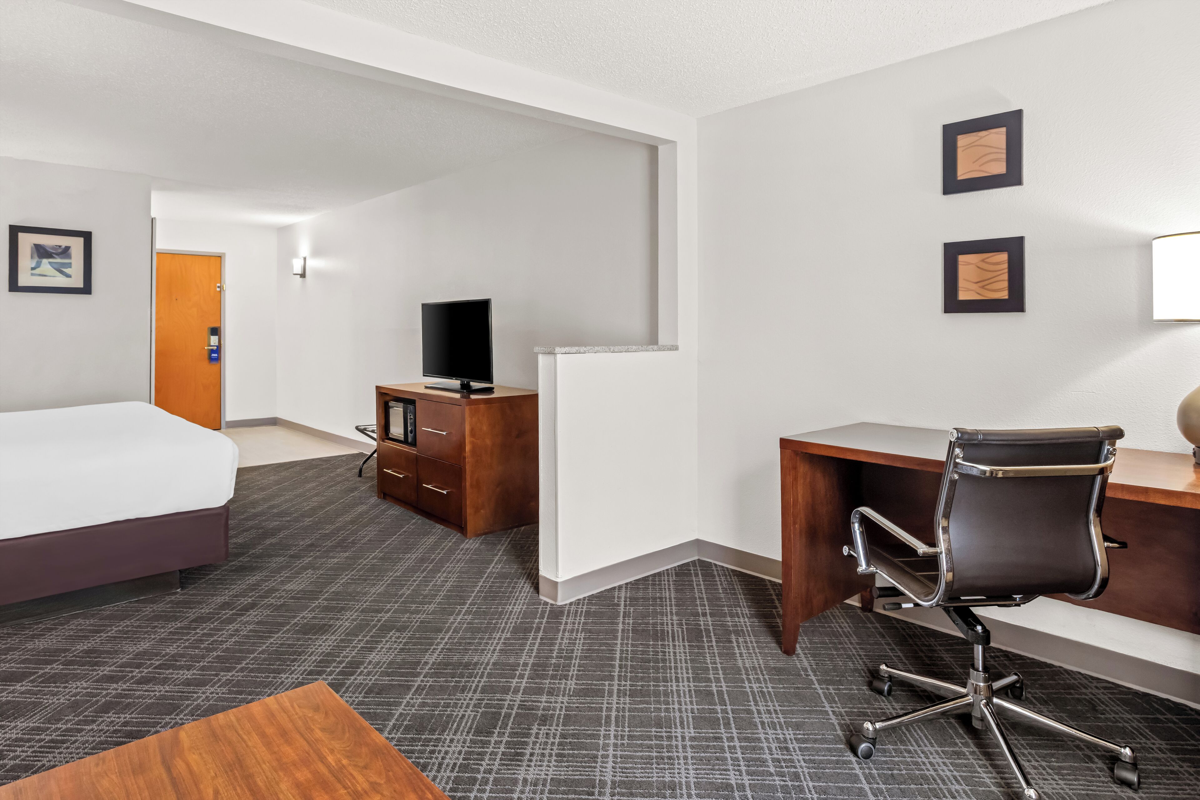 A hotel room with a bed, desk, chair, and a television.