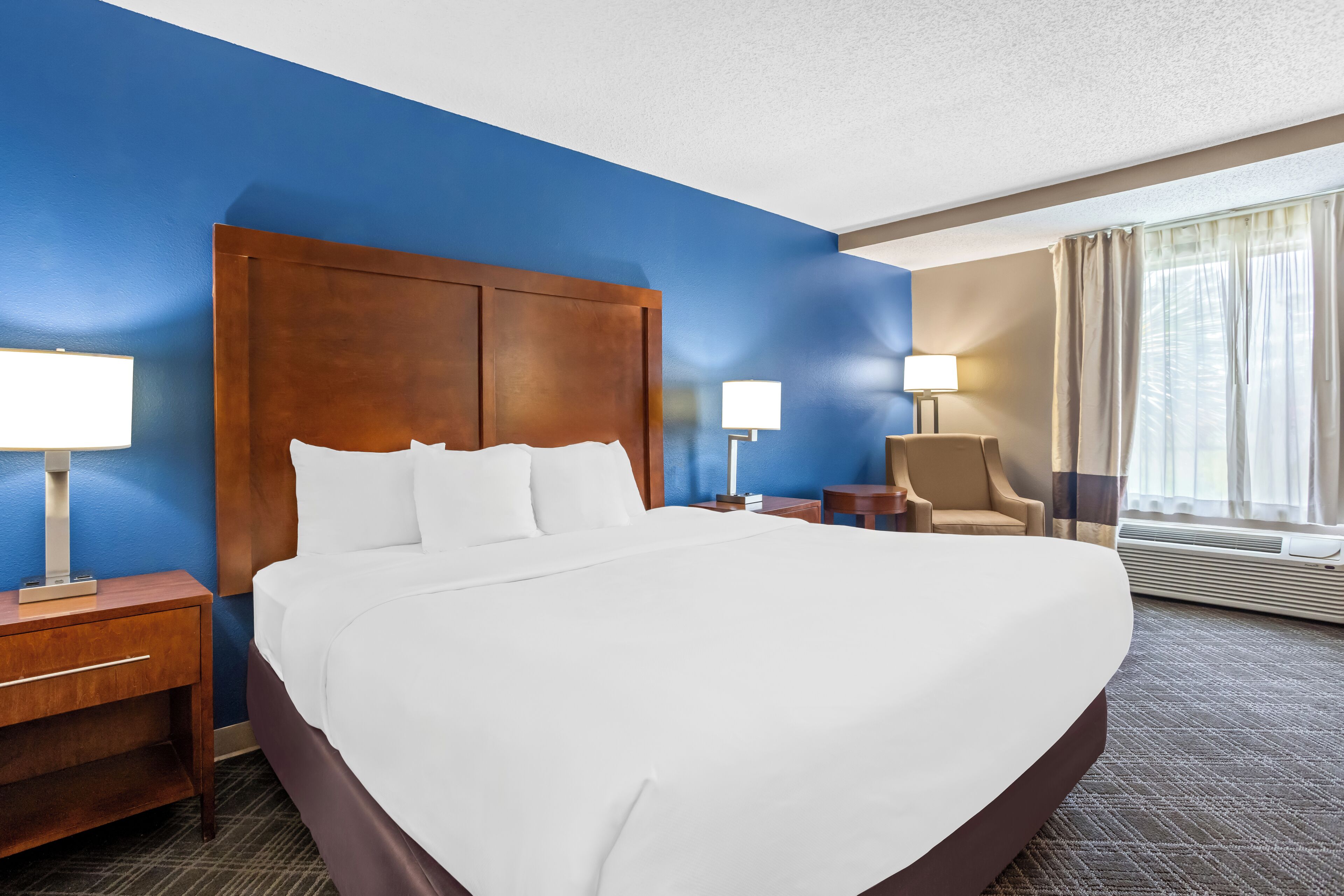 A hotel room with a large bed, two bedside tables with lamps, a chair, and a window with curtains.