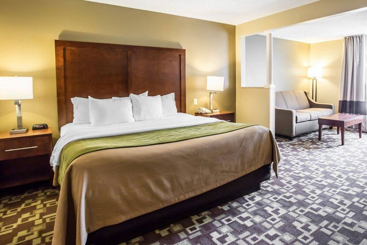 A hotel room with a large bed, bedside tables, a chair, a desk, and a mirror.