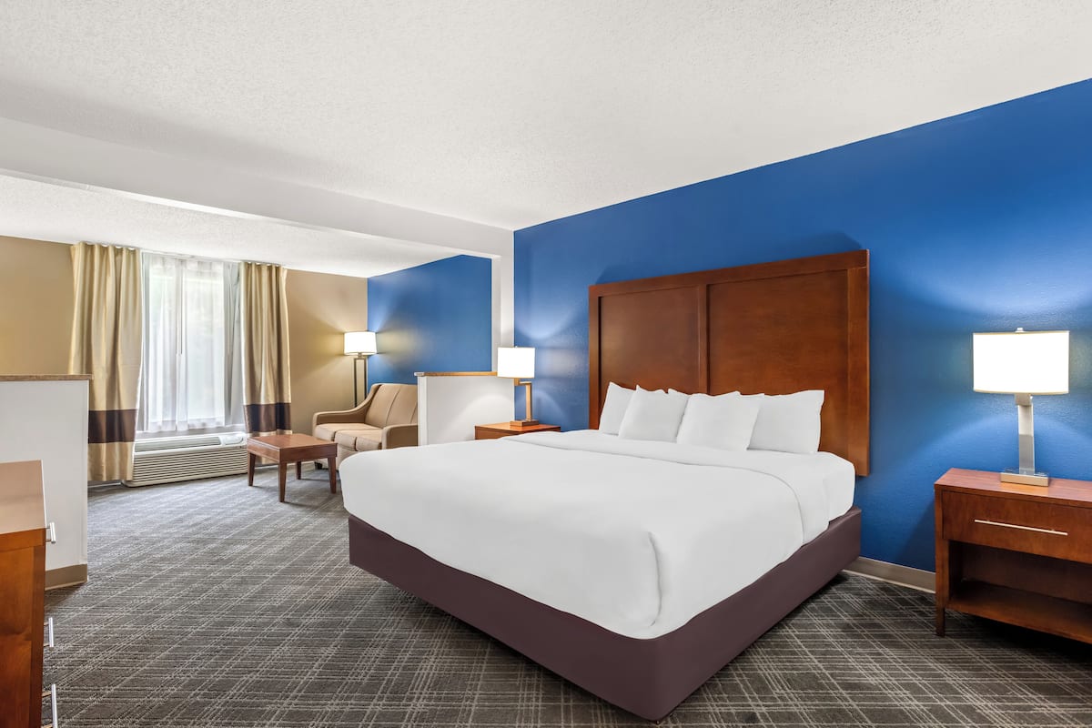 A hotel room with a large bed, a desk, a chair, and a nightstand with lamps.