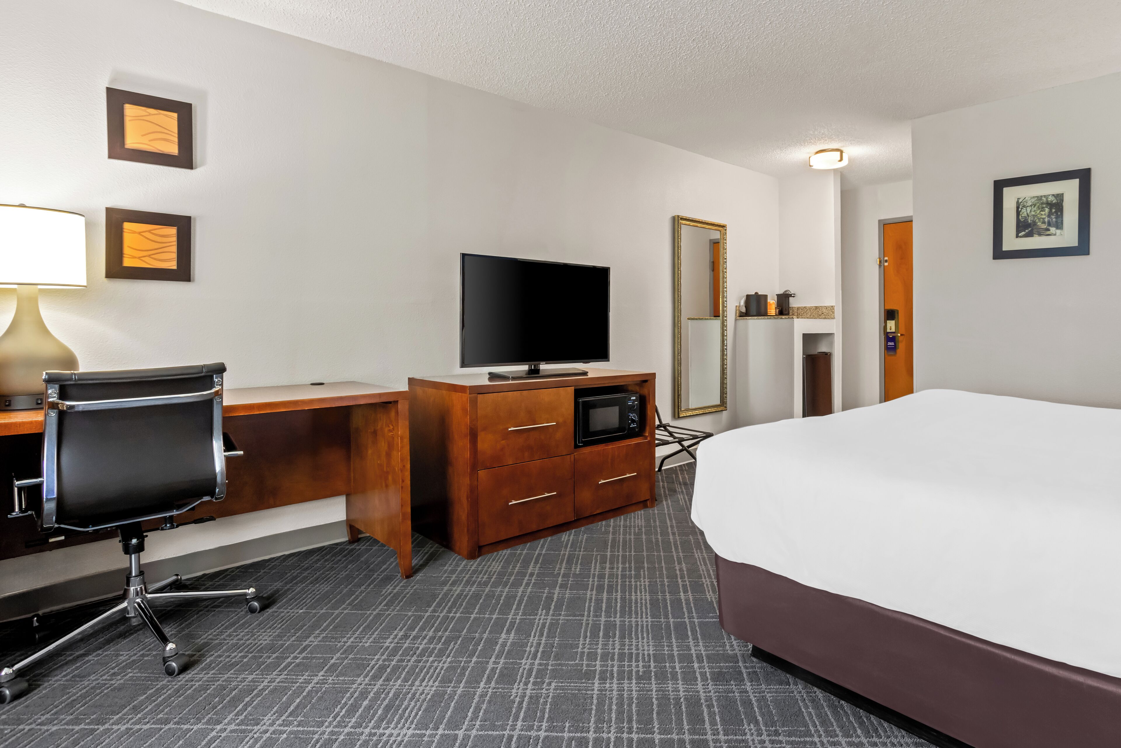 A hotel room with a bed, desk, chair, television, microwave, and a mirror.