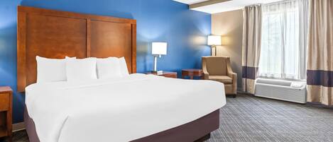 A hotel room with a large bed, a nightstand, a chair, a lamp, and a window with curtains.