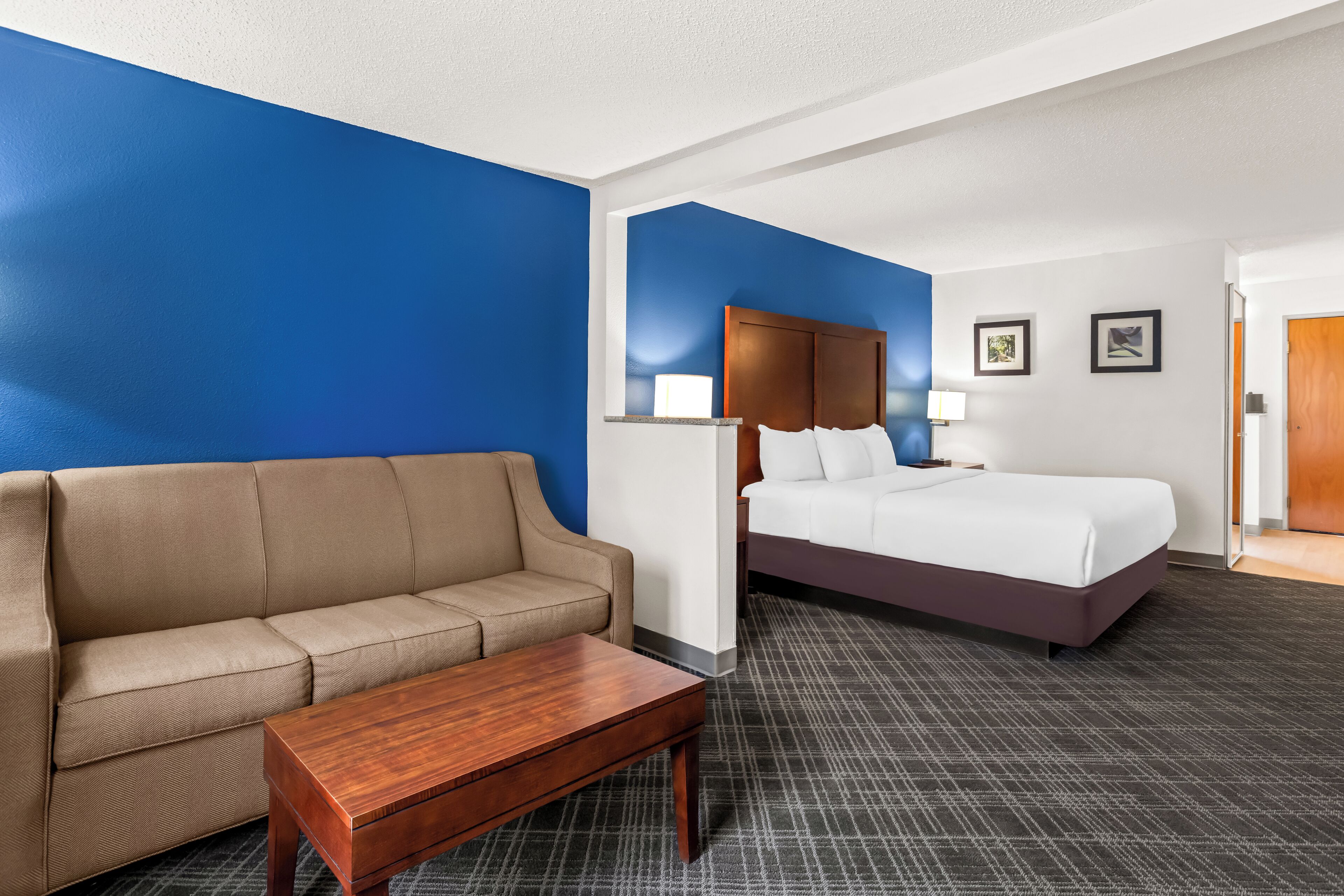 Ein Hotelzimmer mit einem beigen Sofa, einem Holztisch, einem großen Bett mit weißen Leinen und einer blauen Akzentwand.