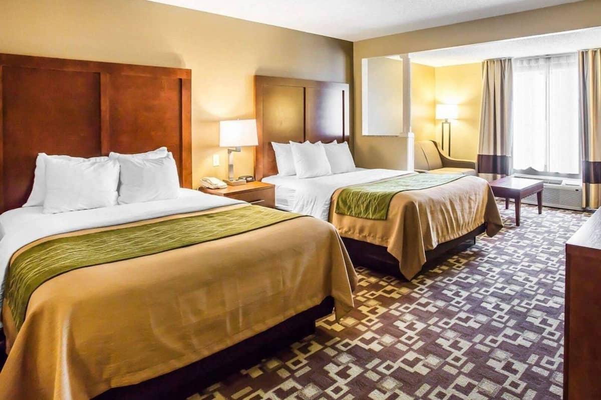 A hotel room with two beds, a desk, a chair, a lamp, and a window with curtains.