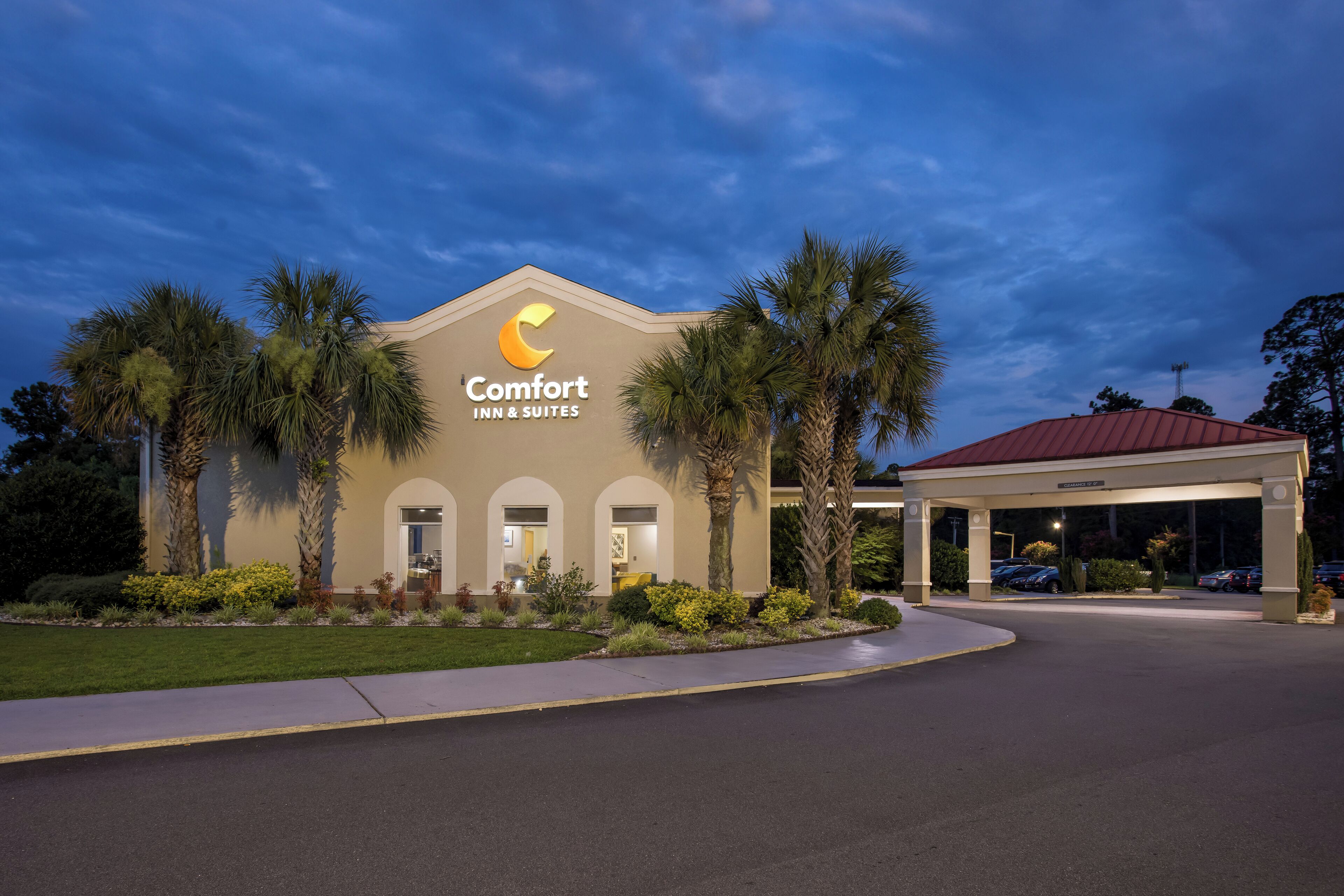 A Comfort Inn & Suites building with a red roof, palm trees, and a well-maintained lawn.