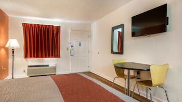 Una habitación de hotel con una cama, un escritorio con dos sillas, un televisor y una puerta.