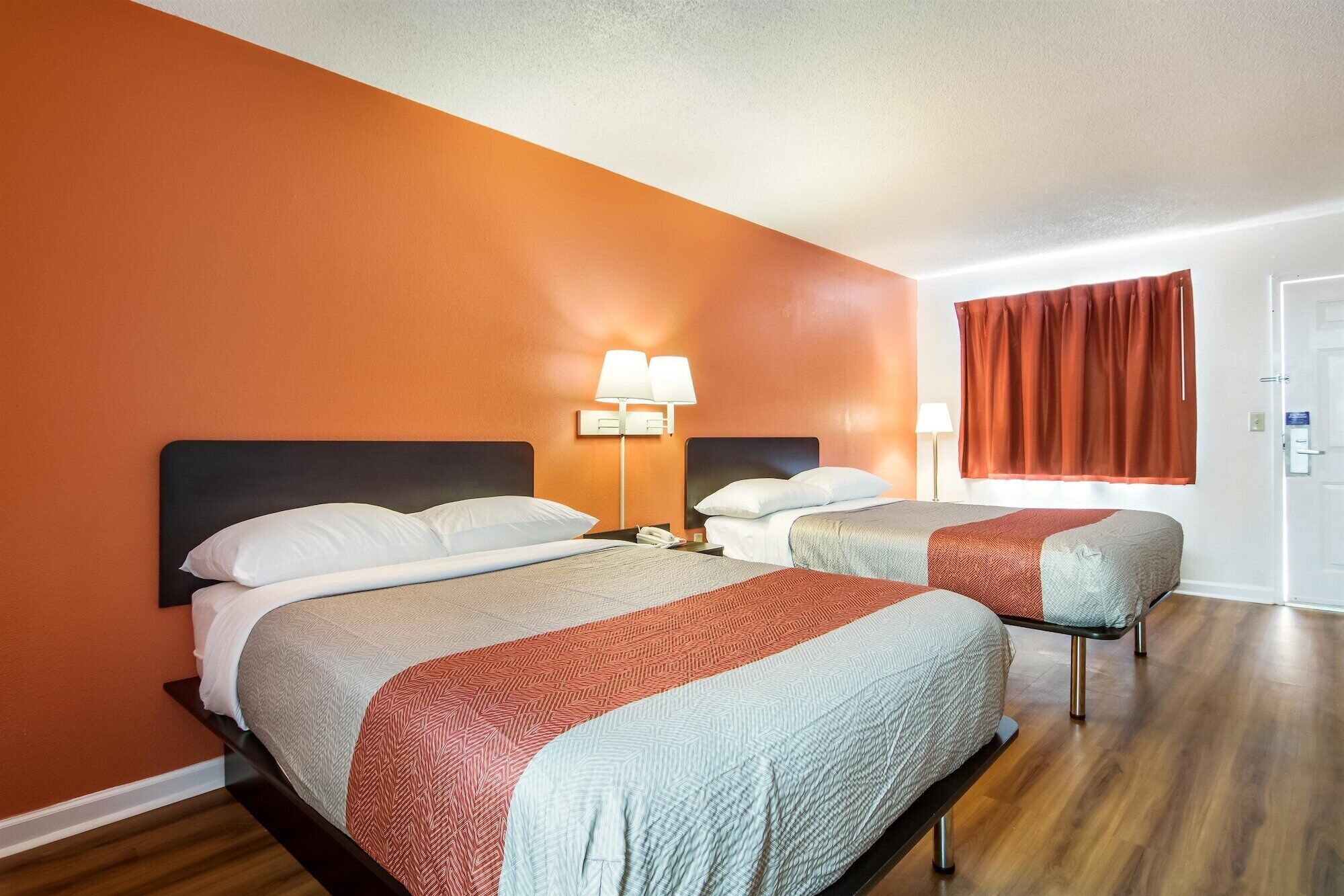 A hotel room with two beds, a nightstand with a lamp, and a window with curtains.