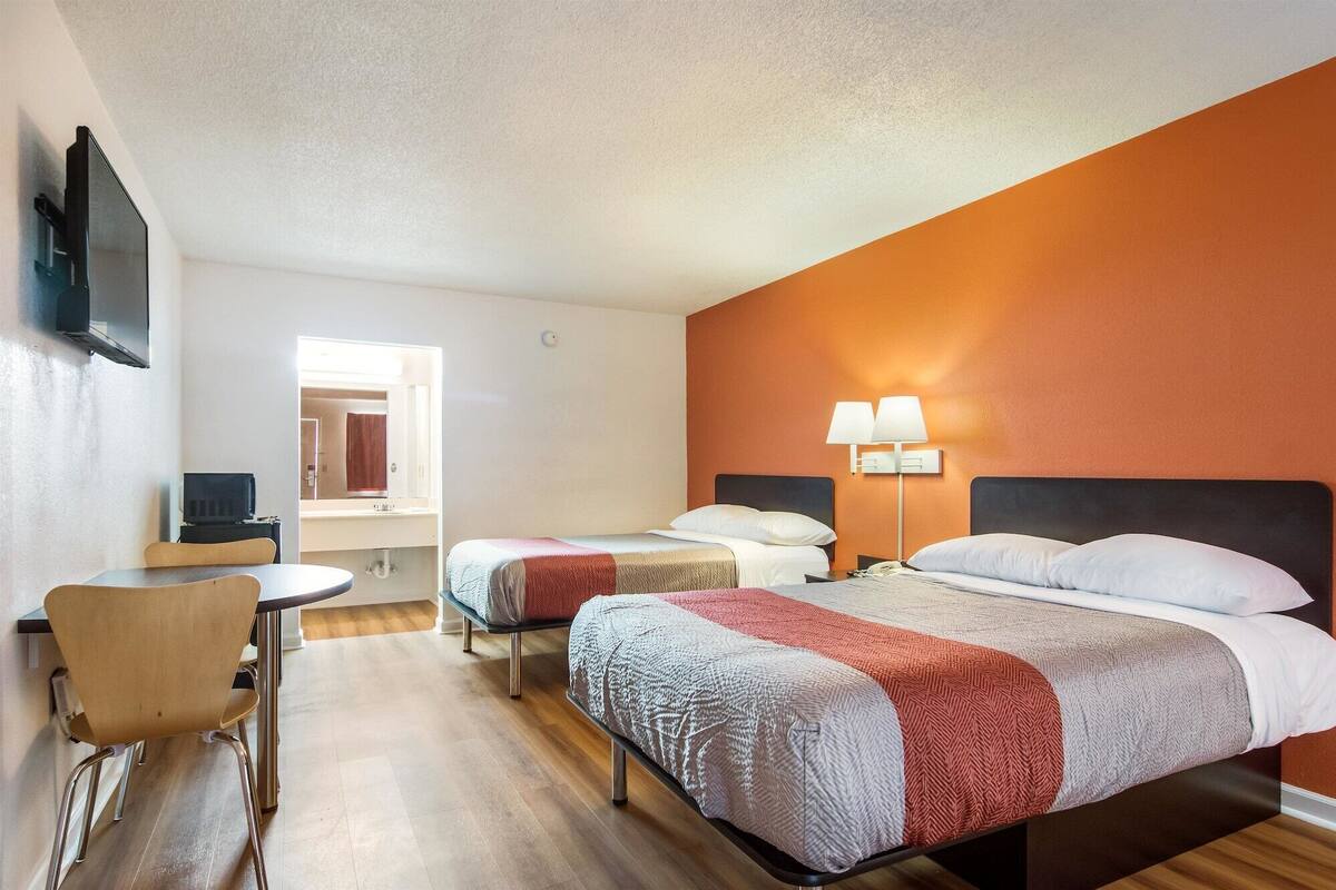 Ein Hotelzimmer mit zwei Betten, einem Schreibtisch, einem Stuhl und einem Fernseher.