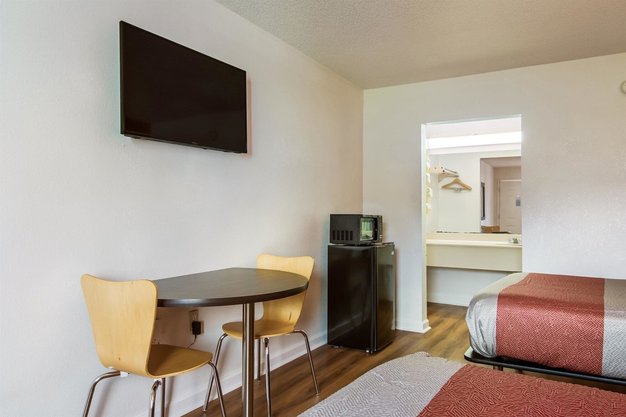 A compact room with a dining table and chairs, a flat-screen TV, a microwave, and a bed with patterned bedding.