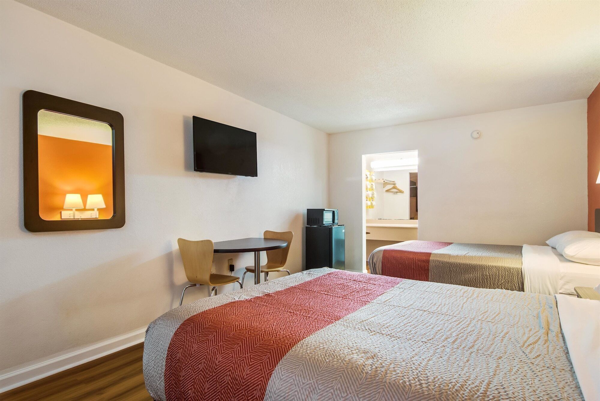 A hotel room with two beds, a desk, a chair, a TV, and a minibar.