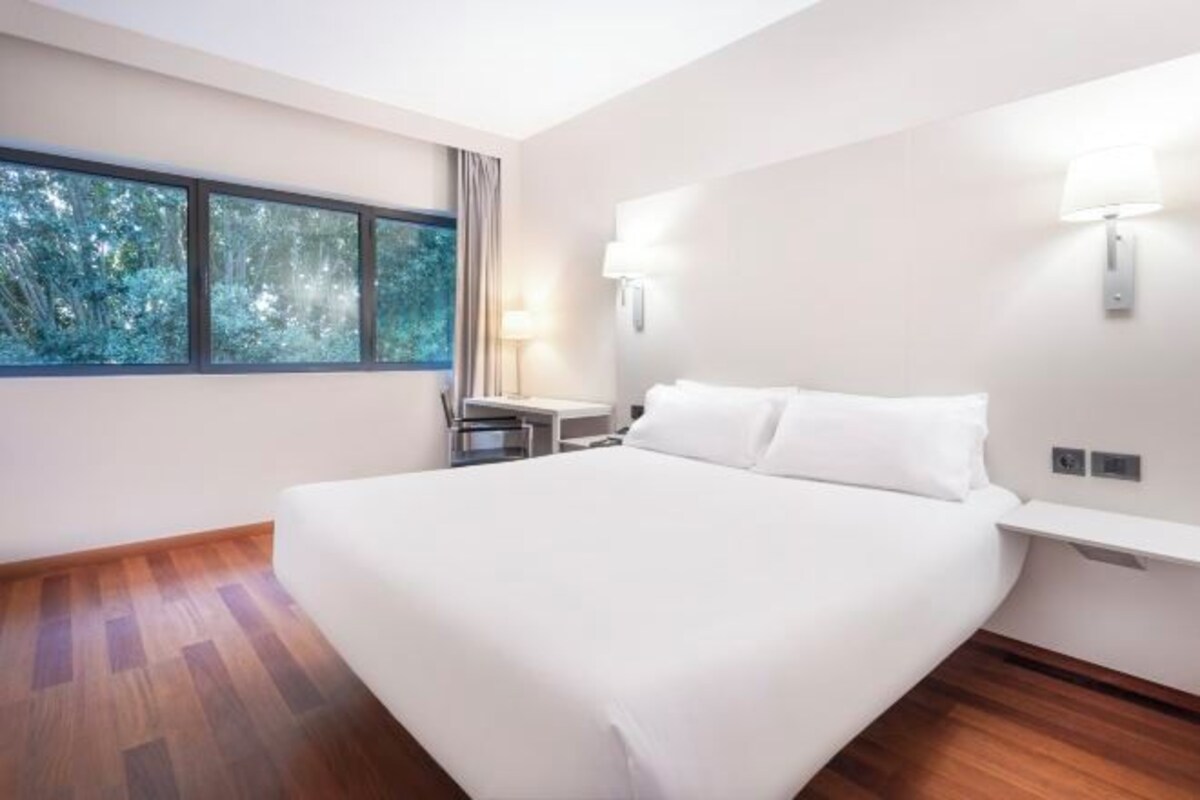 Ein modernes Hotelzimmer mit einem großen Bett, einem Schreibtisch und einem Fenster mit Blick auf Bäume.