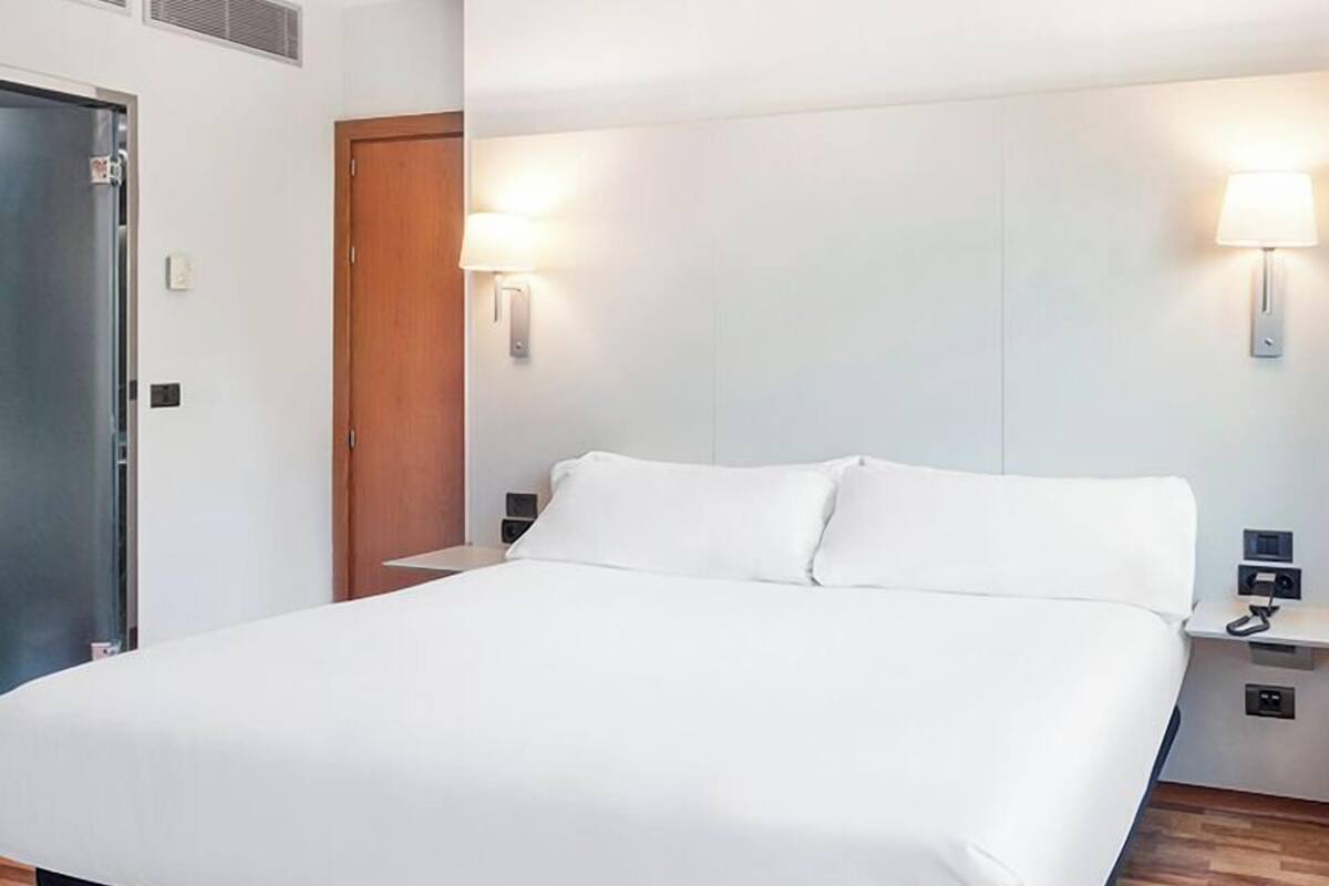 Habitación de hotel con una cama grande, suelo de madera, una puerta de madera y dos lámparas de noche.