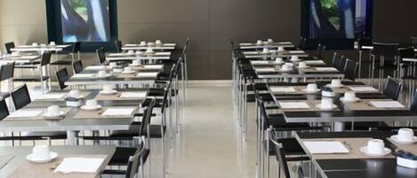 A conference room with rows of tables, each equipped with chairs, plates, and cups.