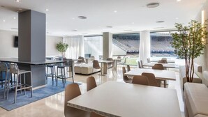 Un espace repas moderne avec des tables et des chaises, un bar et de grandes fenêtres donnant sur un espace extérieur aménagé pour s’asseoir.