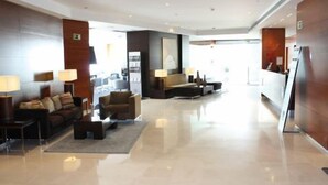 Un hall d’entrée spacieux au design moderne, comprenant un espace salon avec des canapés et des fauteuils, un comptoir d’accueil et un grand miroir.