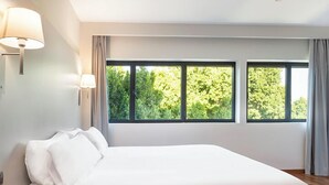 Une chambre à coucher moderne avec un grand lit, une table de chevet et une fenêtre donnant sur des arbres.