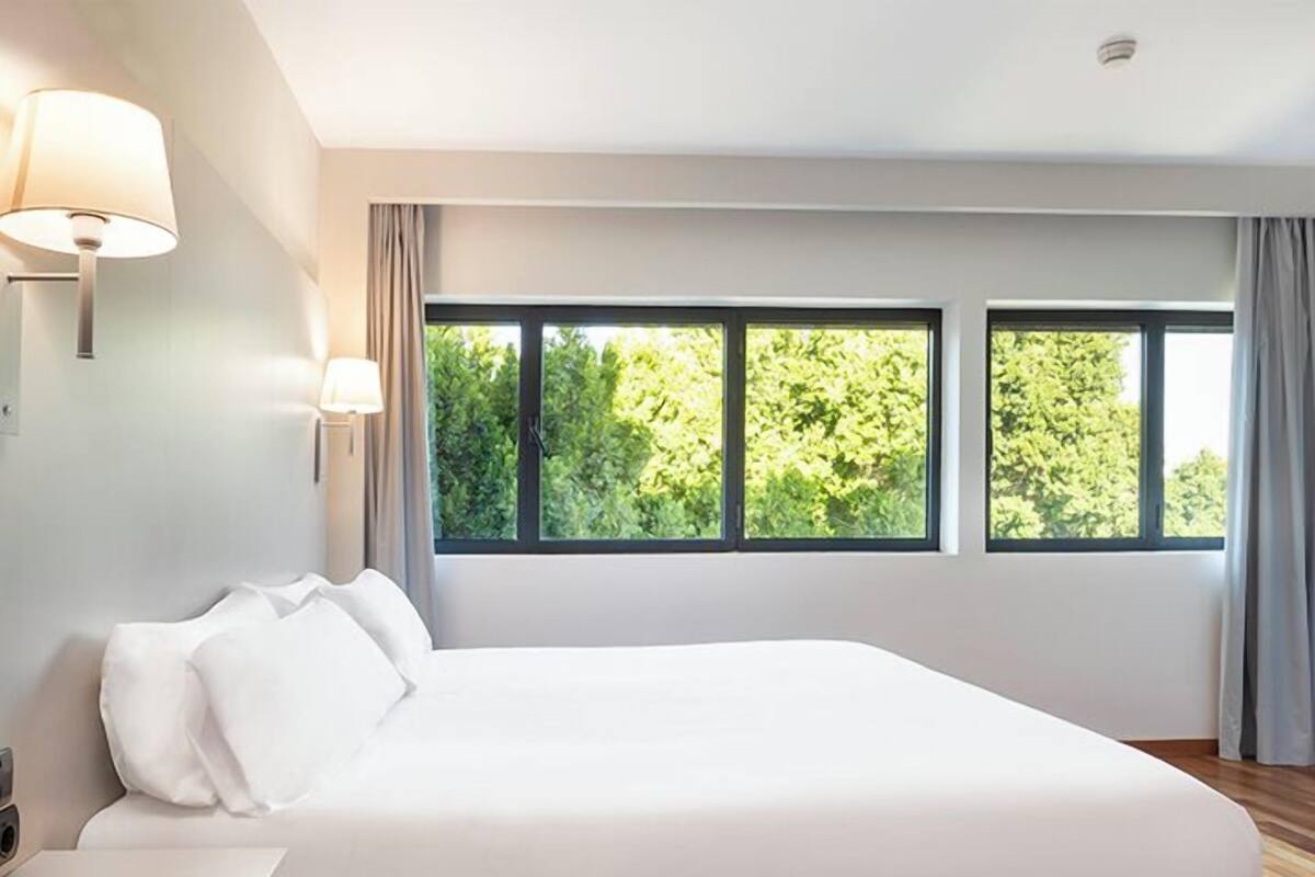 Un dormitorio moderno con una cama grande, una mesita de noche y una ventana con vistas a árboles.