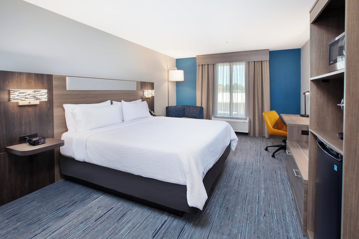 Ett modernt hotellrum med en stor säng, ett skrivbord, en stol, en TV och en minibar.