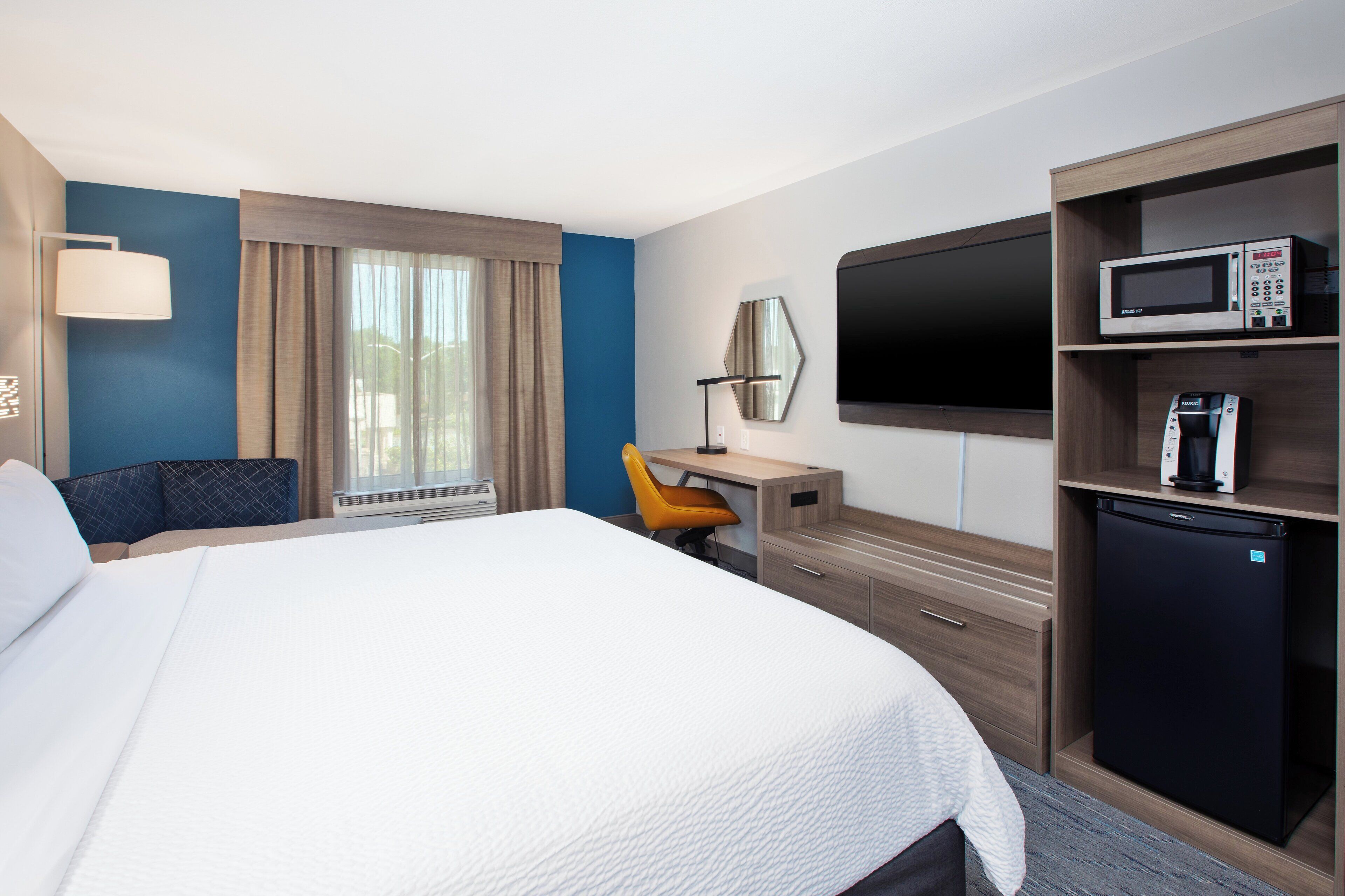 A hotel room with a large bed, a desk with a chair, a television, a microwave, and a refrigerator.