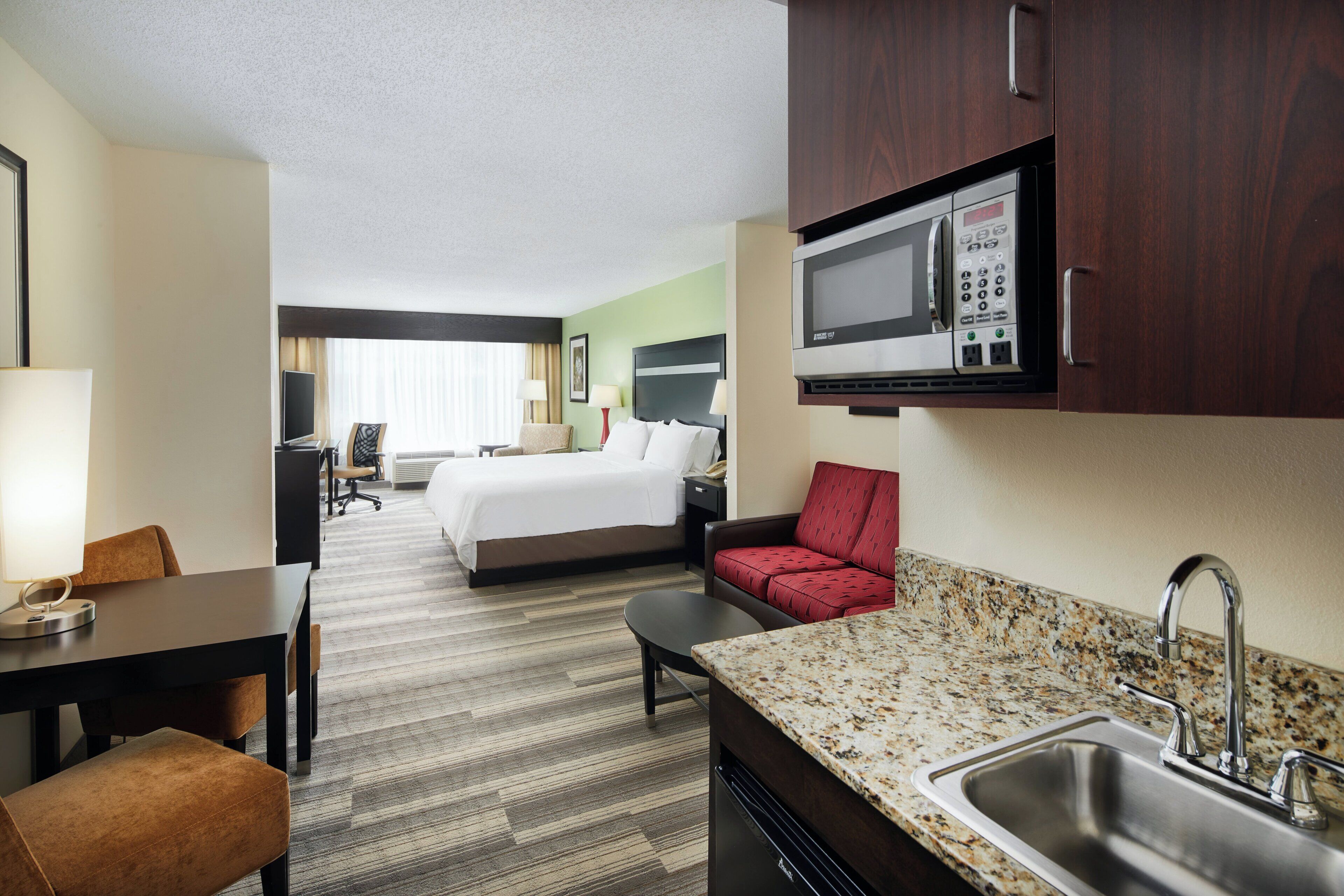 A hotel room with a bed, a desk, a chair, a microwave, and a sink.