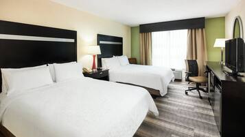 Une chambre d’hôtel avec deux lits, un bureau avec une télévision, une chaise et une table de chevet avec une lampe.