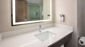 Een badkamer met een wit wastafelmeubel, een grote spiegel en een douchecabine met glazen wanden.