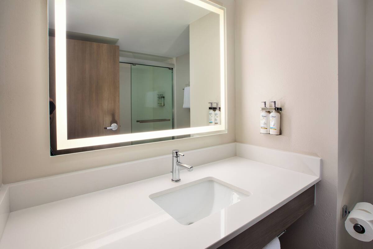 Une salle de bain avec un lavabo blanc, un grand miroir et une douche à parois de verre.