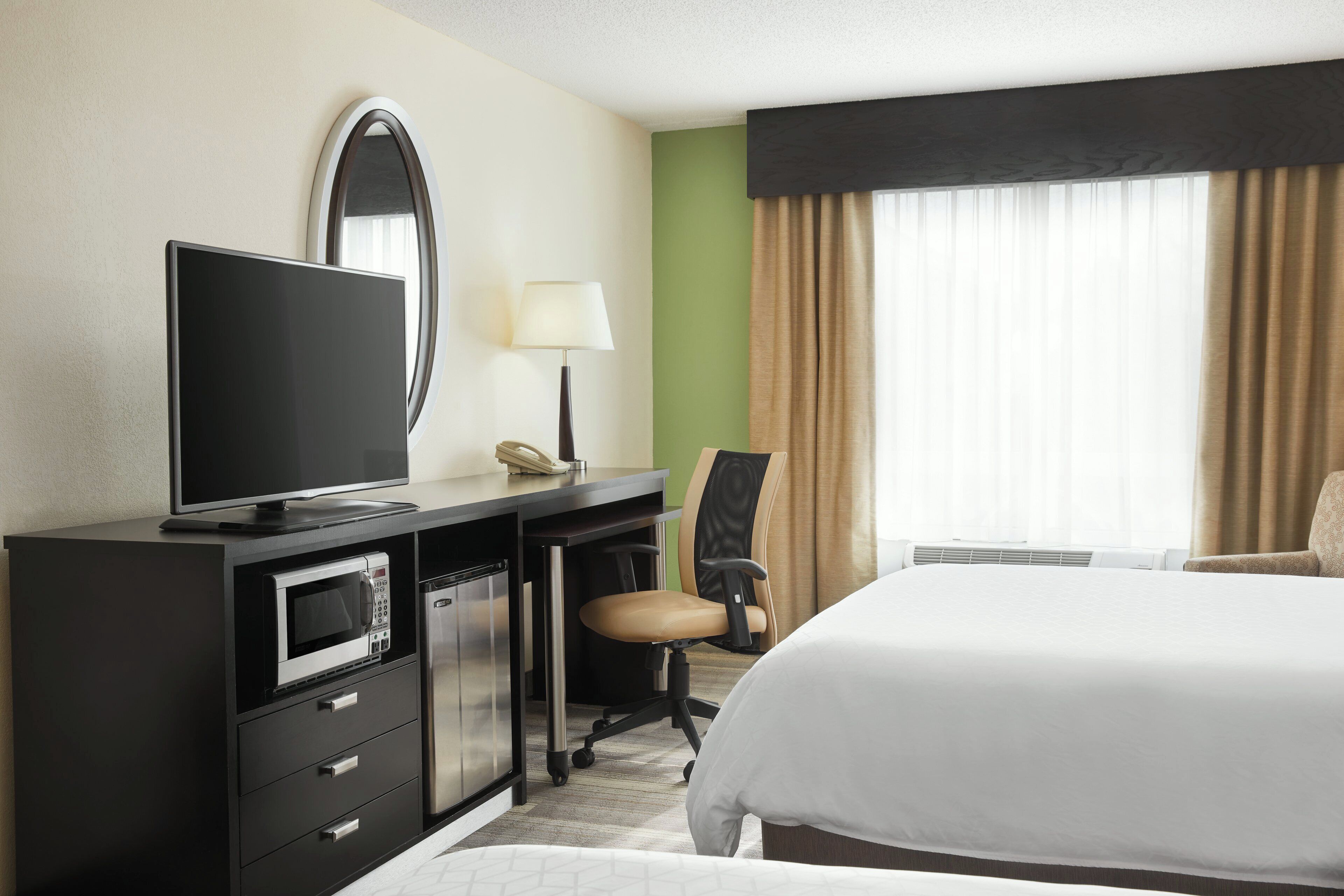 A hotel room with a bed, a desk with a TV, a microwave, a chair, and a lamp.