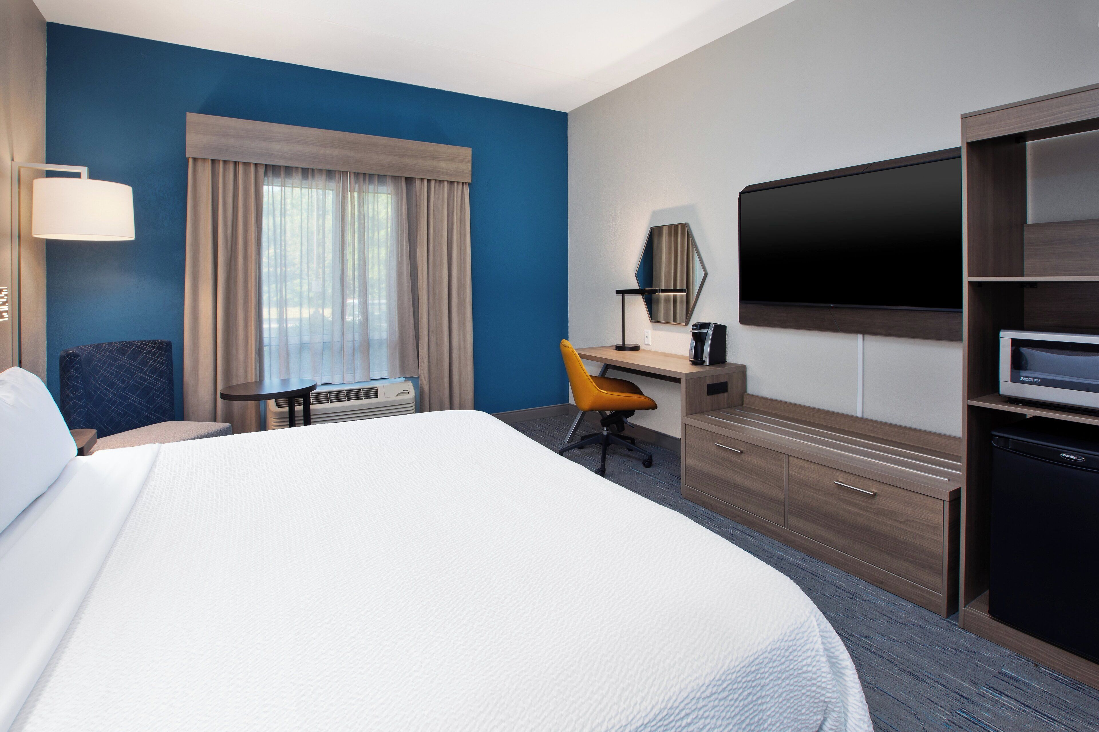 Una habitación de hotel con una cama grande, un escritorio con una silla, un televisor y un minibar.
