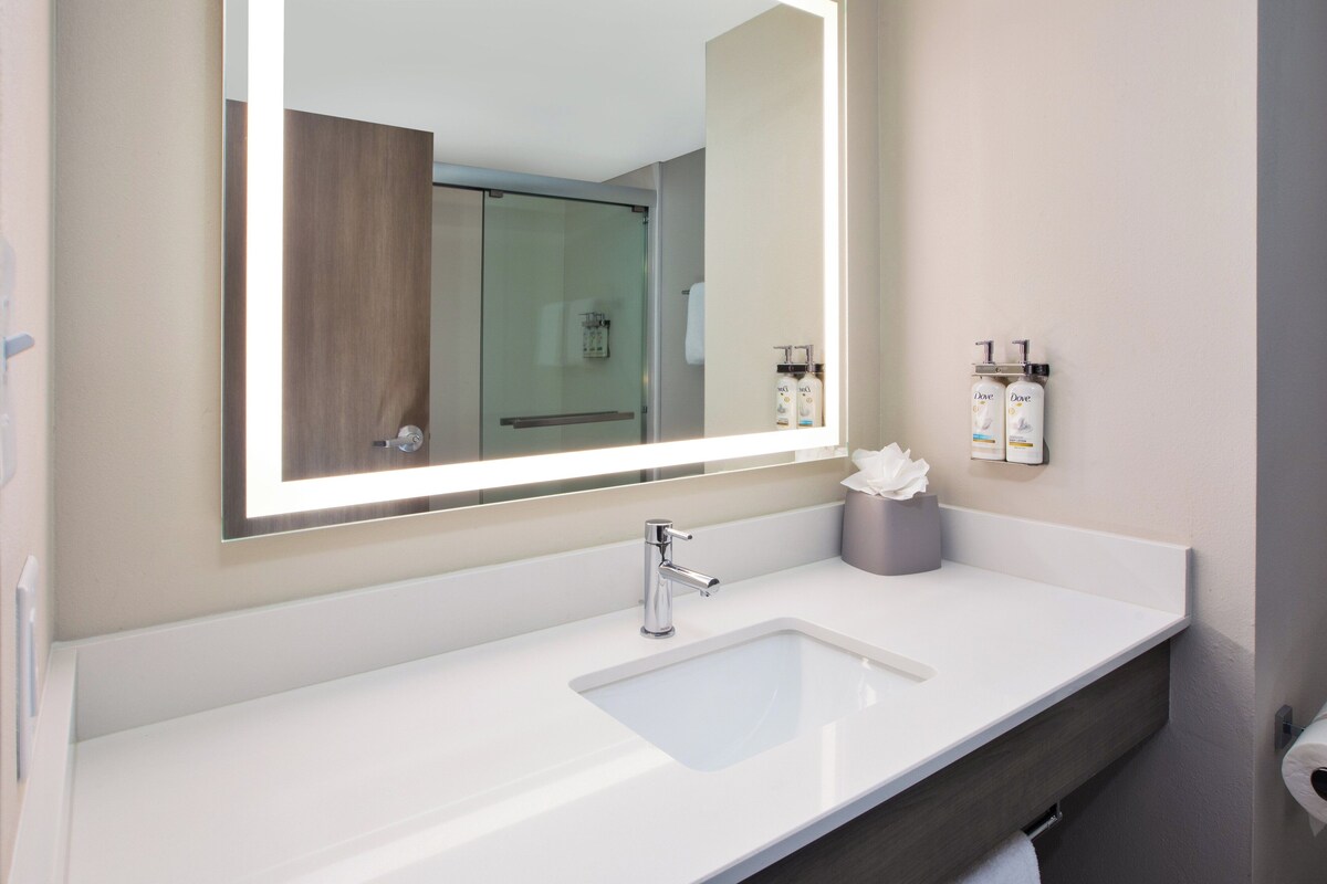 Een moderne badkamer met een grote spiegel, een witte wastafel en twee dispensers voor toiletartikelen.