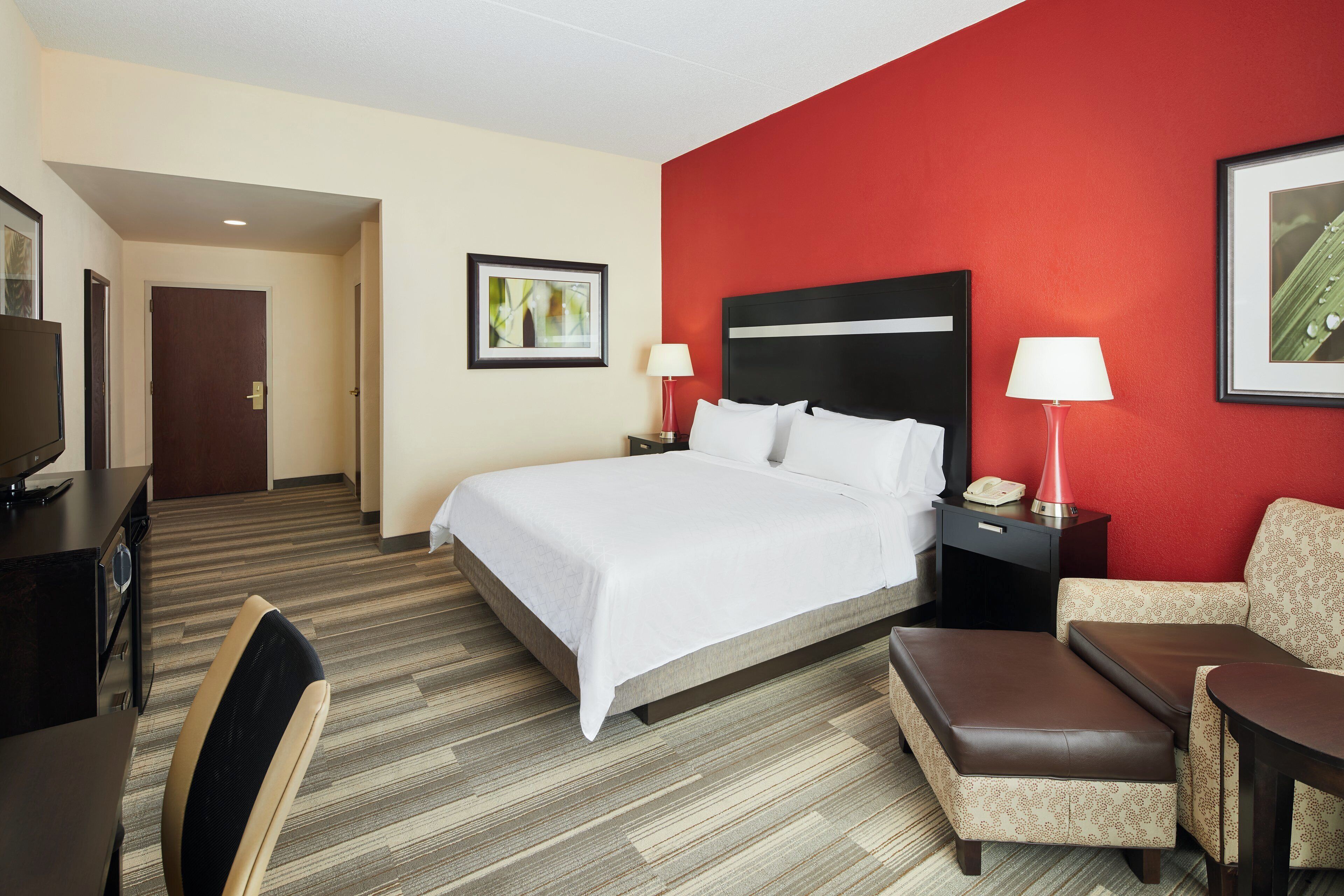 Habitación de hotel con cama, escritorio, silla, lámpara y un cuadro en la pared.
