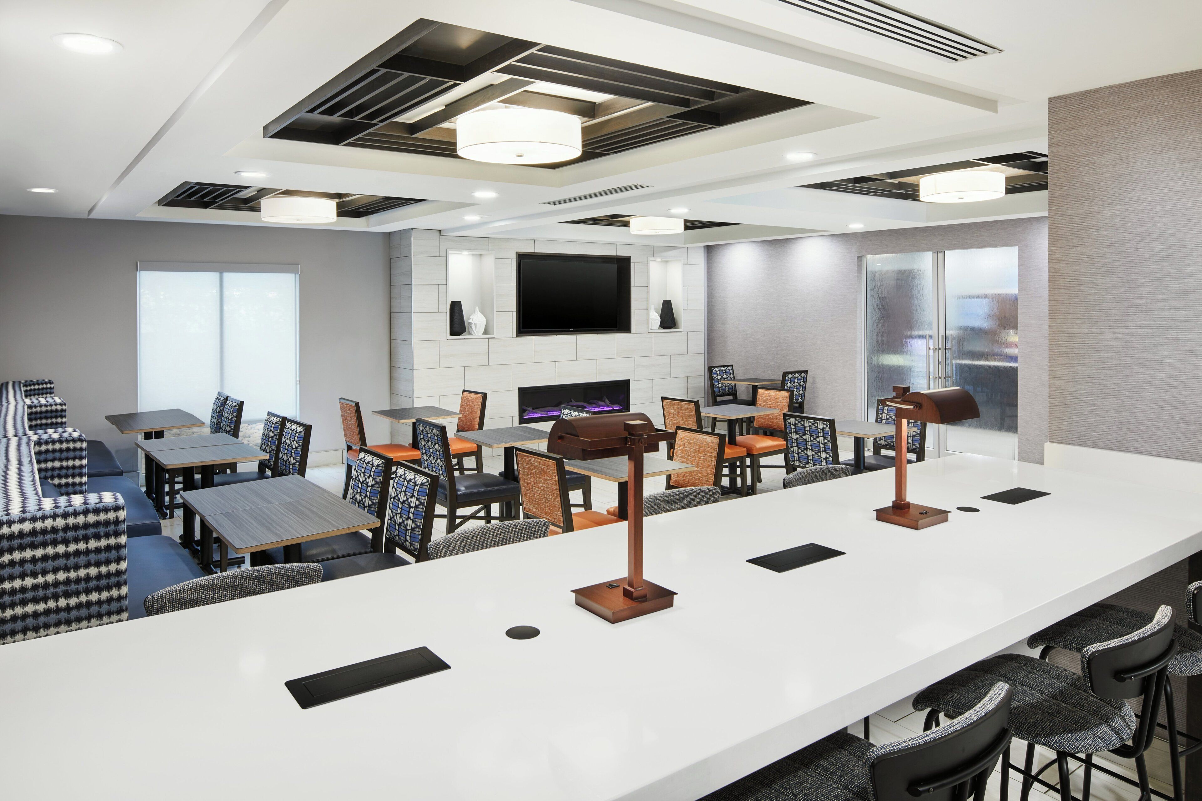 A modern hotel lobby with a bar area, seating arrangements, and a flat-screen TV mounted on the wall.