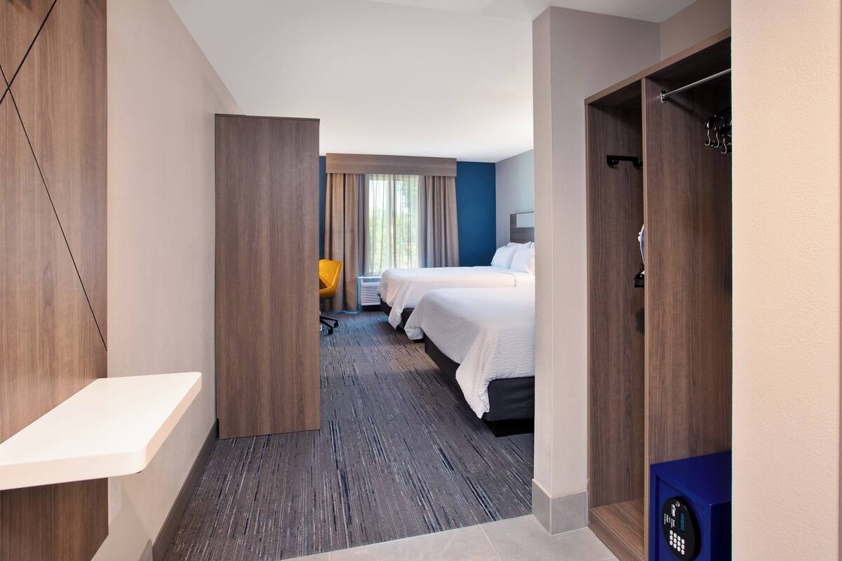 Une chambre d’hôtel avec un plancher en bois, un bureau, une chaise, deux lits et une armoire.