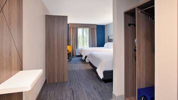 A hotel room with a wooden floor, a desk, a chair, two beds, and a wardrobe.