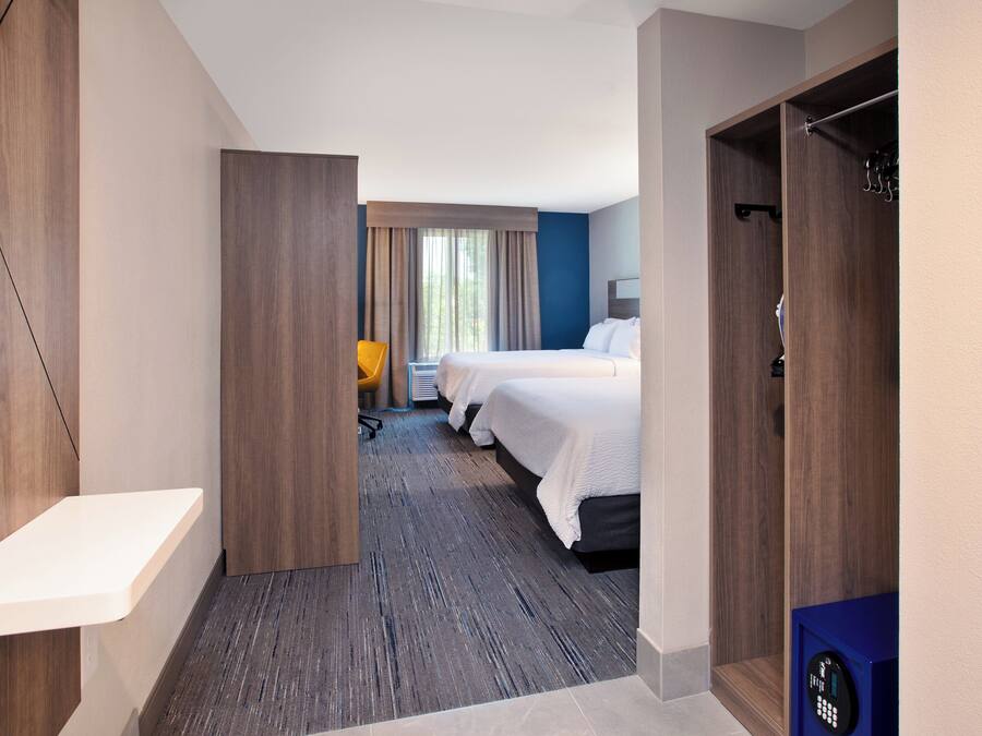 A hotel room with a wooden floor, a desk, a chair, two beds, and a wardrobe.