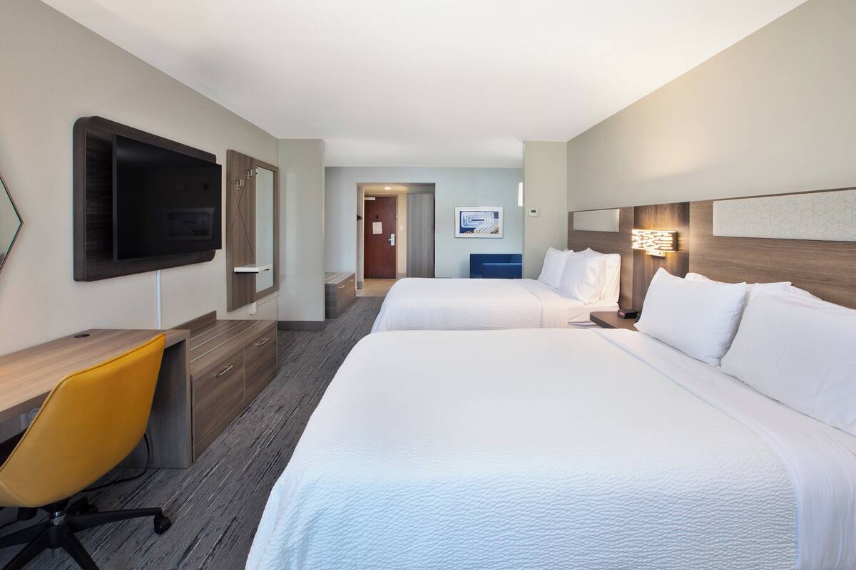 Une chambre d’hôtel avec deux lits, un bureau, une chaise, une télévision et une porte donnant sur une salle de bain.