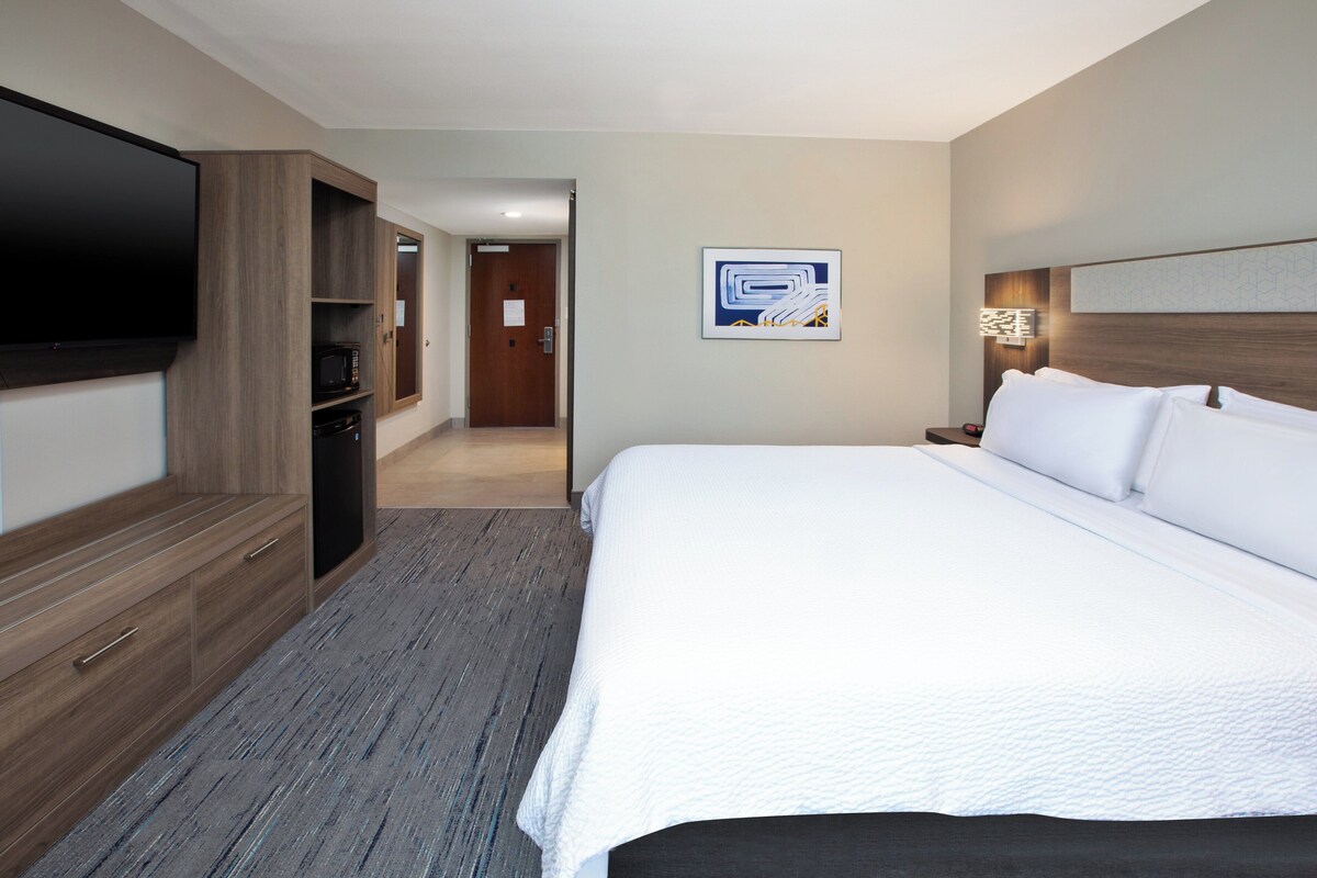 Een hotelkamer met een groot bed, een flatscreen televisie aan de muur, een magnetron en een houten kast.