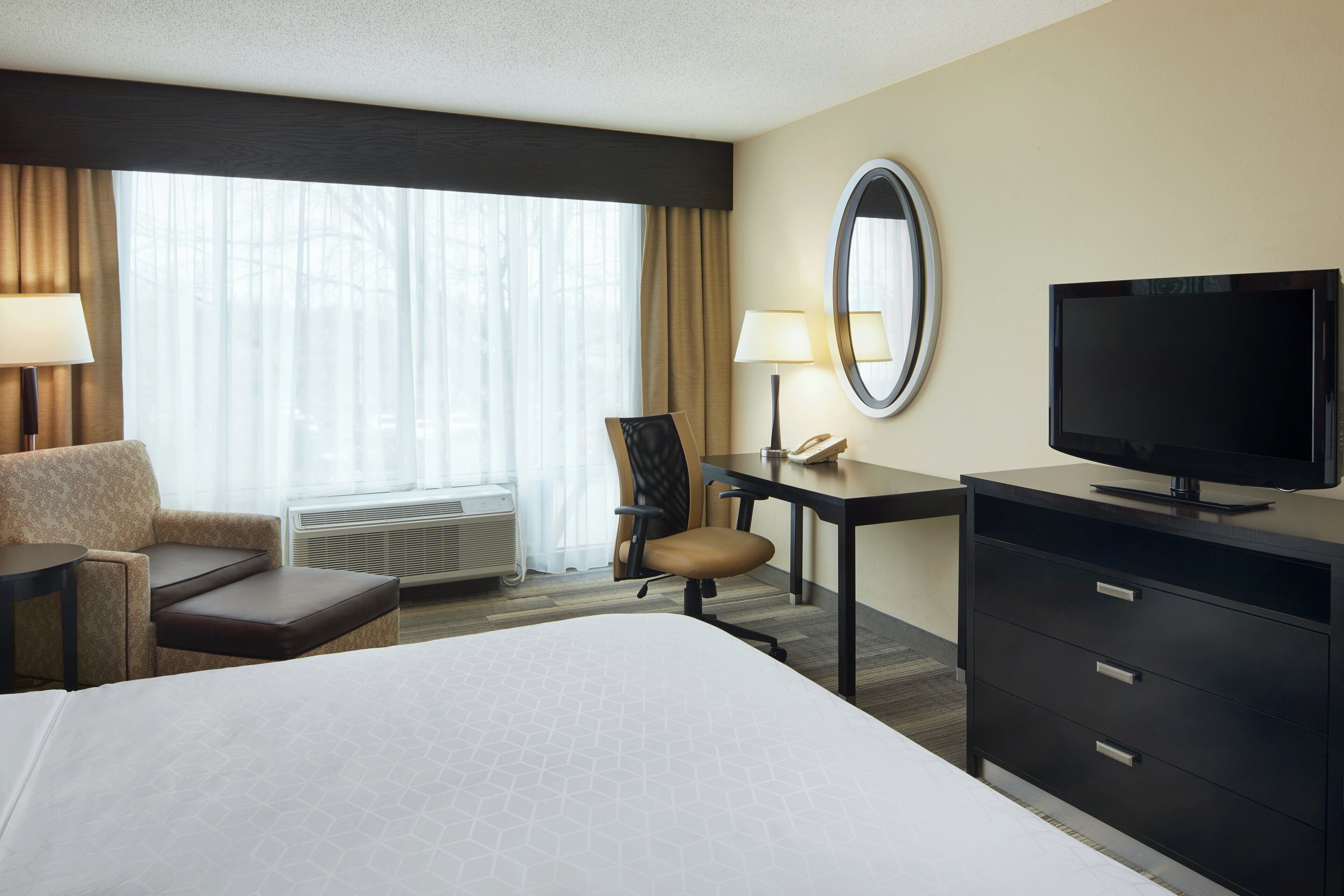 Ein Hotelzimmer mit Bett, Schreibtisch, Stuhl, Fernseher und einem fenster mit Vorhängen.
