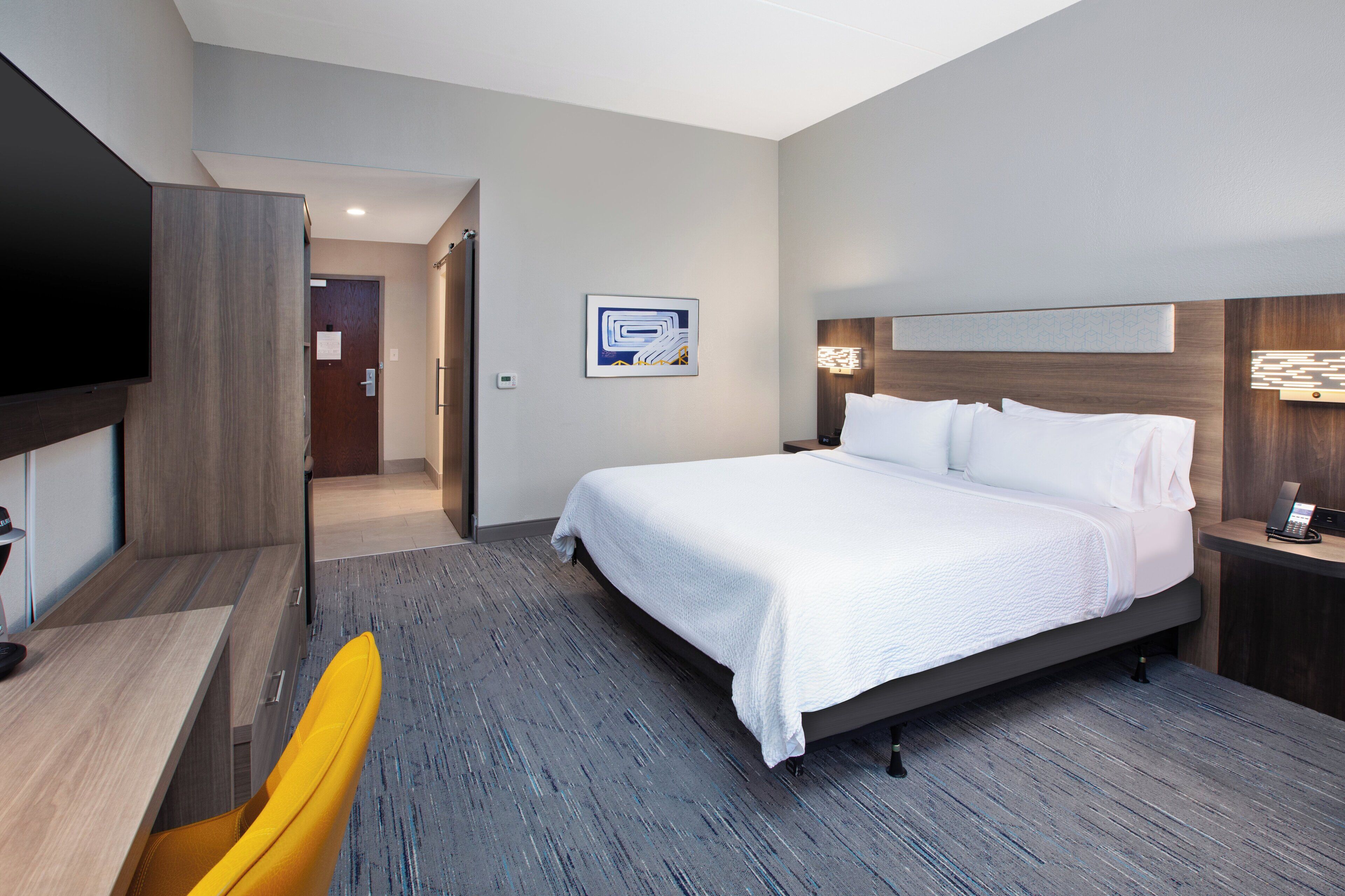 A modern hotel room with a large bed, a desk, a chair, and a flat-screen TV.