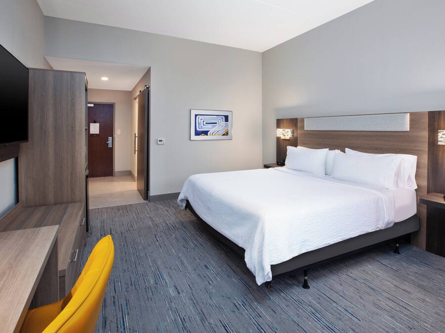 A modern hotel room with a large bed, a desk, a chair, and a flat-screen TV.